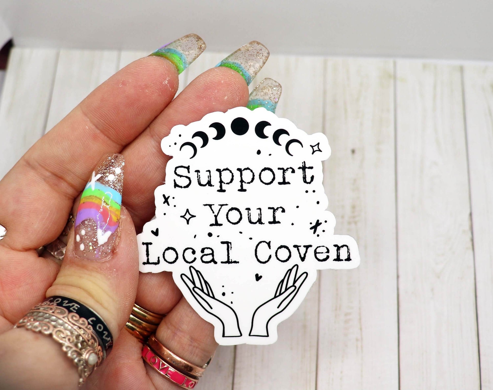 Support Your Local Coven black and white vinyl sticker with moon phases and hands design held in hand with colorful nails