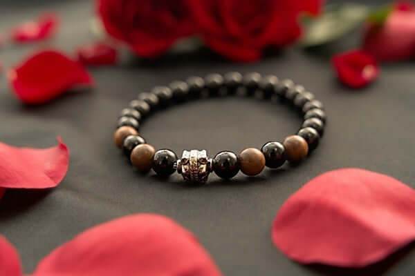 Black onyx and wood beaded bracelet with metal accent surrounded by red rose petals on black surface