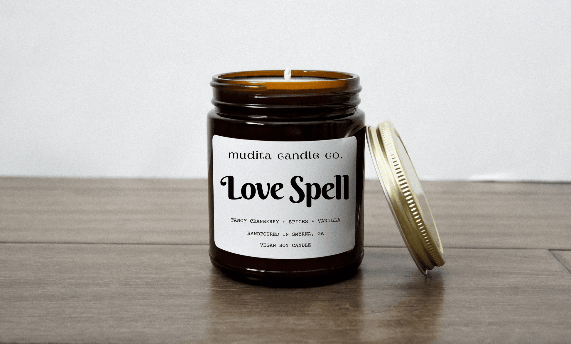 Love Spell vegan soy candle in 9oz amber glass jar with gold lid, scented with tangy cranberry, spices, and vanilla.