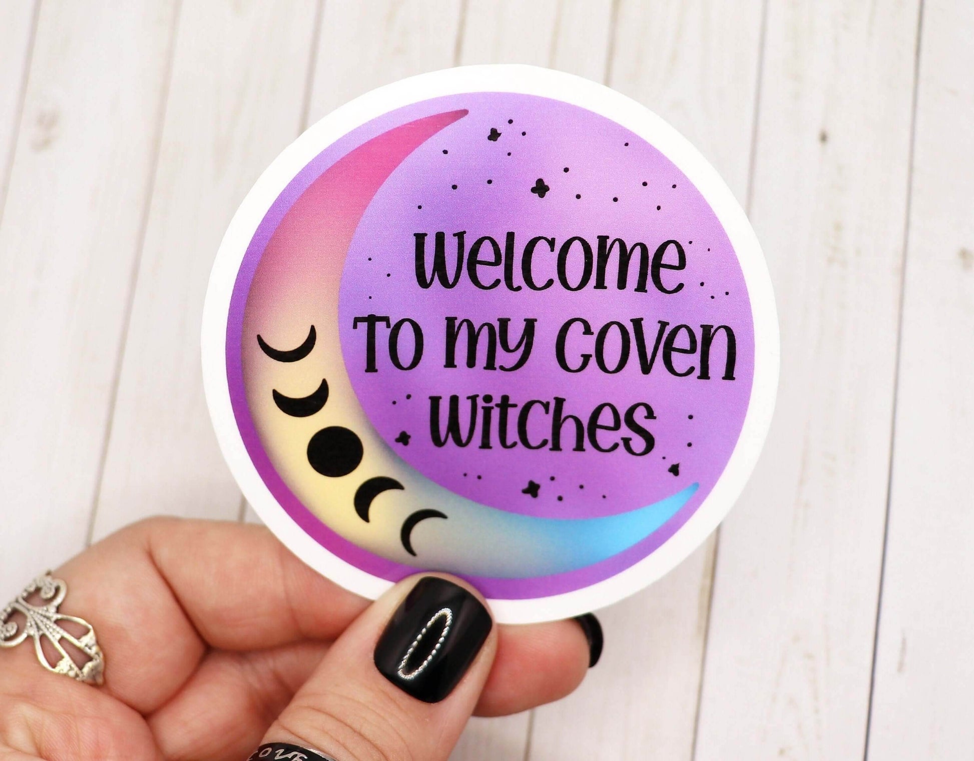 Round vinyl sticker saying "Welcome to my coven witches" with a pastel crescent moon and moon phases on a purple background.