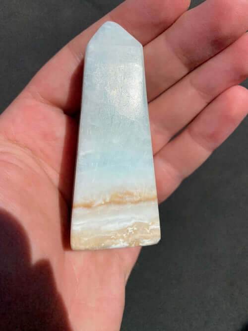 Small Caribbean Calcite Obelisk crystal with blue, green, and yellow hues held in hand, polished for energy cleansing and decor.
