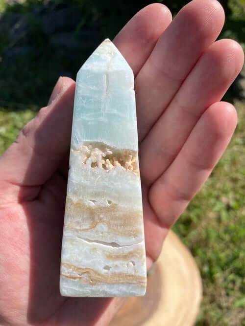 Caribbean Calcite Obelisk crystal with blue, green, and yellow hues held in hand outdoors