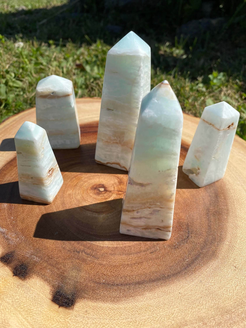 Set of Caribbean Calcite Obelisk crystals with smooth texture and blue, green, and yellow hues on wooden surface outdoors.