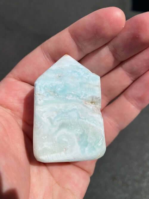 Hand holding a polished Caribbean Calcite Obelisk crystal with light blue and white hues against a dark background