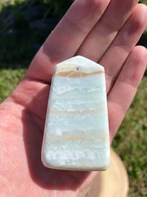 Caribbean Calcite Obelisk crystal with blue and beige bands held in hand outdoors