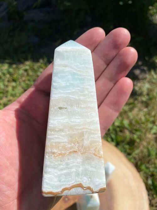 Caribbean Calcite Obelisk crystal with smooth texture and soft blue-green-yellow hues held in hand outdoors