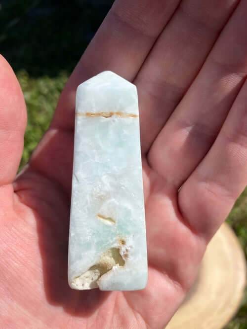 Caribbean Calcite Obelisk crystal with blue and green hues held in hand against outdoor background
