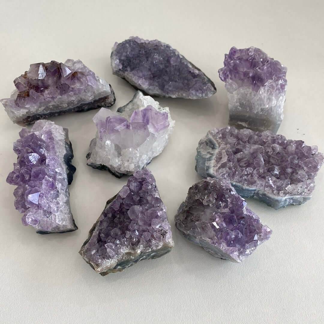 Collection of small purple amethyst clusters with varying shapes and sizes on a neutral background